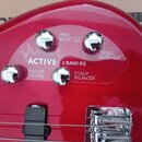 Detail červeného trupu basové kytary s ovládacími prvky. Na povrchu jsou čtyři chromované oválné knofíky a nápisy ACTIVE, 2 BAND EQ, BASS BOOST/CUT,…