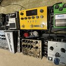 Černý kytarový pedalboard s několika efekty. Jsou zde pedály s nápisy SIMPLIFIER X, BOSS Noise Suppressor NS-2, NUX, Ibanez Tube Screamer, MORLEY a F…