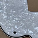 Detailní záběr na bílý pickguard s perleťovým efektem. Materiál má texturovaný, odrazivý povrch a černý lem po obvodu. V plastu jsou vidět vyvrtané o…