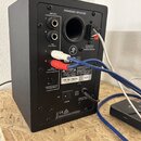 Zadní strana černého aktivního reproduktoru s nápisem POWERED SPEAKER. Jsou zde vstupy TRS (BAL/UNBAL) a RCA (UNBALANCED), výstup OUTPUT TO PASSIVE S…