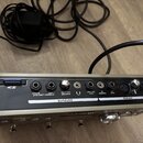 Zadní strana stříbrného elektronického zařízení s panelem označeným nápisy OUTPUTS a INPUTS. Jsou zde vidět konektory s popisky: S2, STEREO LINE OUT…