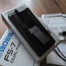 Stříbrný sustain pedál s dvěma černými plasty v horní části. Na boku je uveden nápis BOSS FS-7 DUAL FOOTSWITCH. Povrch pedálu i plastové části vypada…