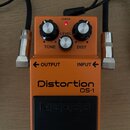 Oranžový kytarový efekt s nápisy Distortion a DS-1. Na horní části jsou tři ovládací knoflíky s popisky TONE, LEVEL a DIST a červená kontrolka s nápi…