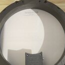Fotografie znázorňuje zadní stranu elektronického bubnu s černým plastovým rámem a bílou membránou. Na černé připojovací části je vidět logo Roland a…