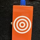 Oranžový efekt pedál s modrým ovládacím knoflíkem. Na přední straně je bílý grafický symbol v podobě soustředných kruhů (terč). Povrch je hladký, bez…