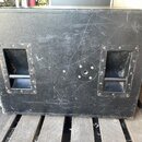 Černý hranatý reproduktorový box s texturovaným povrchem. Na přední straně jsou dvě vestavěné rukojeti v recessed rámech a uprostřed kulatý kovový pr…