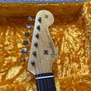 Hlava dřevěné elektrické kytary v žlutém plyšovém pouzdře. Na hlavě je černý nápis Fender a STRATOCASTER s doplňkem WITH SYNCHRONIZED TREMOLO. V horn…