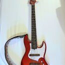 Kytara typu basová v červené metalické barvě s bílým pickguardem. Na hlavě je viditelné logo "Squier". Nástroj má čtyři struny a je vybaven černým po…