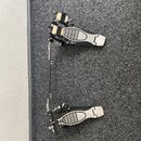 Dvojpedál na bicí buben v černé a stříbrné barvě. Na horním pedálu je viditelný nápis "MASH-UP". Povrch pedálů má stříbrné drážkované gumové nebo kov…