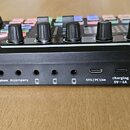 Černý audio mixér s ovládacími knoflíky a barevnými tlačítky. Na zadní straně jsou nápisy Condenser mic, Headset, Earphone, Accompany, OTG / PC Live…