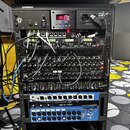 Černý rack s řadou audio zařízení na kolečkách. V horní části jsou vidět nápisy SAMSON a PG-2 TYPE F, dále jednotka s červeným digitálním displejem z…