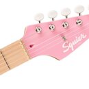 Detail hlavy růžové elektrické kytary se světlým hnedem hmatníku. Na hlavě je bílý nápis Squier a pod ním menší text BY FENDER, v pravém horním rohu…