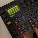 Černý digitální sampler a drum computer značky Elektron, model Digitakt. Zařízení má podsvícený displej s nápisem SUBAQUATIC, několik otočných potenc…