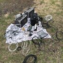 Sada audio vybavení rozložená na bílé plátno na trávě. Soubor obsahuje dva šedé reproduktory, jeden z nich v transportním kufru, malý mixovací pult a…