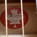 Detail vnitřní štítku akustické kytary s červeným kruhem a bílým javorovým listem. Na štítku je nápis Norman, Est. 1972 Québec, Canada, fait à la mai…