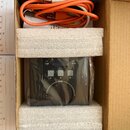 V kartonové krabici s polystyrenovými vložkami je černý elektronický přístroj zabalený v plastové fólii. Na horní hraně zařízení jsou nápisy USB a MI…