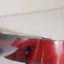 Detailní pohled na hranu korpusu strunného nástroje v červené barvě s přechodem do modré. Povrch je lakovaný a vykazuje odlesky. Na hraně je viditeln…