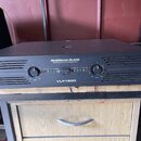 Černý výkonový zesilovač v kovovém šasi s nápisy AMERICAN AUDIO a PROFESSIONAL POWER AMPLIFIER. Na předním panelu je uprostřed označení modelu VLP150…