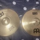 Dvě mosazné činely s koncentrickým drážkováním, položené na šedé plišové přikrývce s bílými tečkami. Oba činely mají černý nápis HCS a logo MEINL ve…