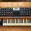 Černý analogový syntetizátor s dřevěním šasi a klaviaturou. Na horním panelu jsou nápisy LFO, MODULATION BUSSES, OSCILLATORS, MIXER, FILTERS, ENVELOP…