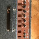 Detailní pohled na ovládací panel basového komba v hnědé barvě s černými knoflíky. Panel obsahuje přepínač ACTIVE/PASSIVE, vstup INPUT a ovladače VOL…