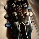 Fotografie zachycuje hlavu černé elektrické kytary s nápisy Gibson a Les Paul MODEL v žluté barvě. Na hlavě jsou vidět stříbrné ladičky a kovové stru…