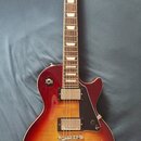 Elektrická kytara s trupem v červeno-žlutém sunburst provedení a hnědým hmatníkem s trapezoidními vložkami. Na hlavě je nápis Gibson, modelové označe…