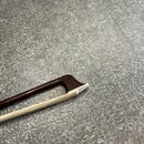 Detailní pohled na hrací hůlku smyčcového nástroje. Hůlka je vyrobena z tmavě hnědého dřeva s bílou koncovkou v místě připojení smyčce. Povrch dřeva…