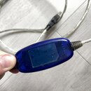 Modrý průhledný plastový modul s integrovaným digitálním displejem, který je součástí stříbrného pleteného kabelu. Na modrém plastu jsou vidět drobné…