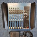 Modrý mixovací pult s nápisem YAMAHA a označením modelu MG12/4. Zařízení obsahuje několik kanálů s posuvníky, otočnými knoflíky a tlačítky v červené…