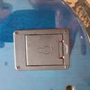 Detail zadní strany modrého nástroje s viditelným kovovým krytem elektroniky. Na šedém plastovém víčku je vyraženo logo v podobě stylizované osmičky…
