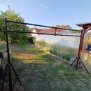 Černý kovový stojan na noty nebo vybavení s horizontální tyčí a dvěma tripodními nohami. Konstrukce je z kovových trubek s viditelnými spojovacími šr…