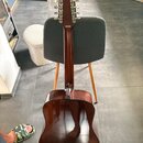 Zadní strana akustické kytary v tmavě hnědé barvě s lakovaným povrchem. Na hlavě nástroje jsou vidět stříbrné ladičky a nápis MADE IN JAPAN. Kytara j…