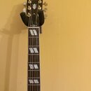 Fotografie zachycuje hmatník a hlavu elektrické kytary v držáku. Na hlavě je nápis Gibson a logo ve tvaru koruny. Hmatník má tmavé dřevo s bílými tro…
