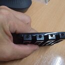 Detailní pohled na černý kovový kobylík kytary držený v ruce. Kobylík obsahuje šest sedel s imbusovými šrouby pro úpravu výšky. Povrch je černý, s vi…