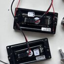 Dvě černé obdélníkové šasi s vnitřními elektronickými součástmi a připojenými červeno-černými vodiči. Na horním modulu je nápis Hybrid Differential P…