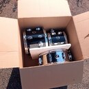 V otevřeném kartonovém boxu jsou tři černé bubny s chromovaným kováním. Na každém z nich je viditelné kulaté logo s nápisem "Pearl". Povrch nástrojů…