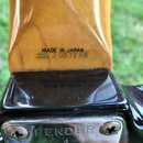 Detail zadní části krku a hlavy kytary. Na dřevěném krku je černý nápis MADE IN JAPAN a pod ním sériové číslo J 007248. Spodní černý lakovaný povrch…