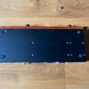 Fotografie zachycuje spodní stranu černého elektronického zařízení s červeným horním okrajem. Na spodním černém povrchu jsou vidět čtyři gumové nožič…