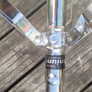 Detail chromovaného kovového stojanu s rozkládacími nohami. Na trubici je viditelný černý štítek s bílým nápisem "enium" a drobným textem "www.denium…
