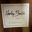Fotografie detailu bílého štítku s černým textem. Na štítku je kurzívou napsán název Harley Benton a pod ním text est. 1998. Ve spodní části je uvede…