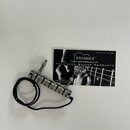 Kovový tremolo systém pro kytaru s černým přívodním kabelem. Vedle nástavce leží vizitka s nápisy BRENNER™, WWW.BRENNERUSA.COM, PRECISION GUITAR PROD…