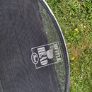 Detailní záběr na černý tlumicí textil s bílým potiskem. Na logu je uveden nápis MUFFLE HEAD a v malém oválu slovo Beat. Povrch látky vykazuje drobné…