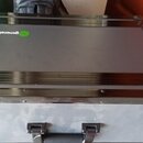 Šedý transportní kufr s kovými hranami a rohovými zpevněními. Na horní části je umístěno zelené kulaté logo a nápis generation. Povrch kufrů vykazuje…