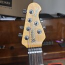 Fotografie zachycuje hlavu elektrické basy z přírodního světlého dřeva. Na povrchu jsou nápisy StingRay a MUSIC MAN s logem ve tvaru písmene M. Jsou…