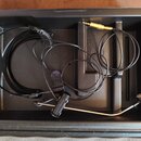 Černý plastový kufřík s vnitřními přihrádkami, ve kterém se nachází headset s mikrofonem. Sestava obsahuje tenký černý kabel, mikrofonní rameno s čer…