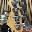 Zadní strana hlavy basové kytary z přírodního dřeva se čtyřmi chromovanými ladičkami. Na dřevě je černý nápis „Designed and based by Fender Crafted i…