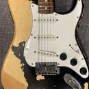 Elektrická kytara typu Stratocaster s černým lakem a bílým pickguardem. Lak na těle je výrazně odloupaný, což odhaluje světlé dřevo. Nástroj má tři s…