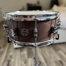 Hnědý dřevěný malý buben s chromovanými obručemi a mechanismy. Na korpusu je kulatý černý štítek s bílým nápisem pdp LIMITED EDITION dw. Povrch dřeva…