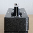 Černý efekt pedál s texturovaným povrchem. Na horní straně je umístěn černý otočný knoflík s bílou značkou, pod ním je nápis loop level. V pozadí je…